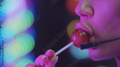Sexy woman with plump lips sucking a lollipop in neon lighting  photo