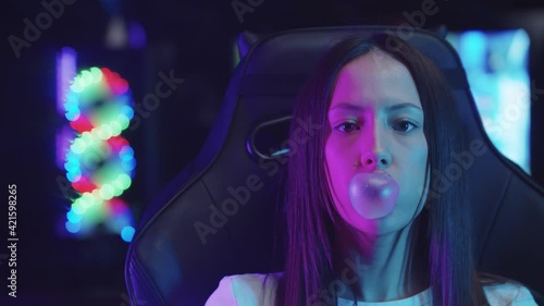 Girl gamer sitting in a chair in gaming club and blowing a bubble gum  photo