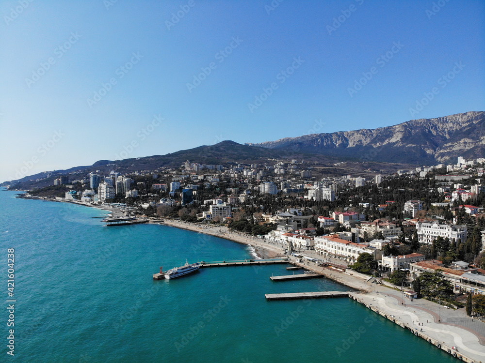 Aerial top view of waterfront and pier with yachts of resort city of Yalta, Crimea at sunny spring day, sea and mountain view. Photo made by drone from above