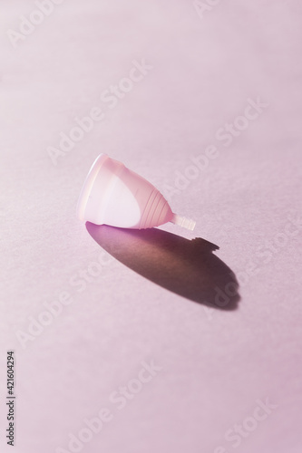 Pink menstrual cup on light pink background. Hard sunlight and shadows