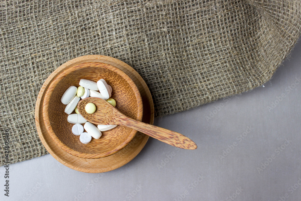 A handful of pills in a wooden plate with spoon, on burlap. The concept of medcine, treatment. Top view. A handful of pills in a wooden plate with spoon, on burlap. The concept of medcine, treatment. Top view.
