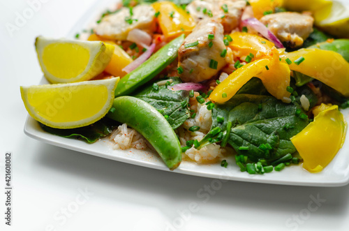 Cooked chicken breast pieces with peppers, sugar snap peas, and baby leaf spinach in a spicy sweet and sour sauce with fragrant rice