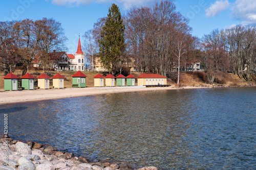 Colorful bath cabins lined up next to sandy beach numbered in roaman numbers with city of Hjo in background, Sweden