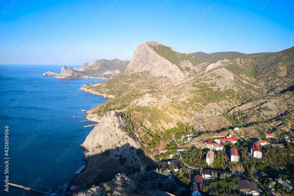 Obraz premium The rocky coast of the sea with a settlement and a mountain road. Shooting from a drone.