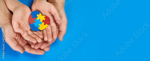 World Autism Awareness day, mental health care concept with puzzle or jigsaw pattern on heart with child and adult hands