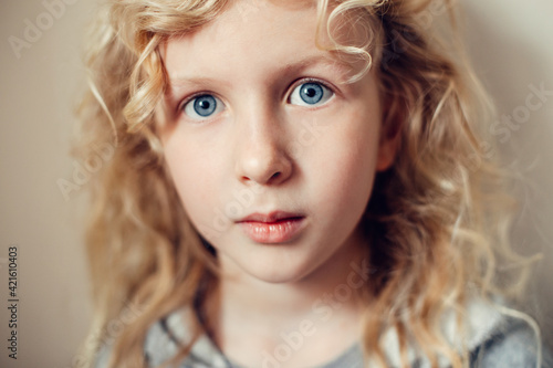 Closeup portrait of beautiful pensive serious Caucasian blonde girl with long hair on light neutral beige background. Pretty real girl child with natural emotions. Happy authentic childhood lifestyle.