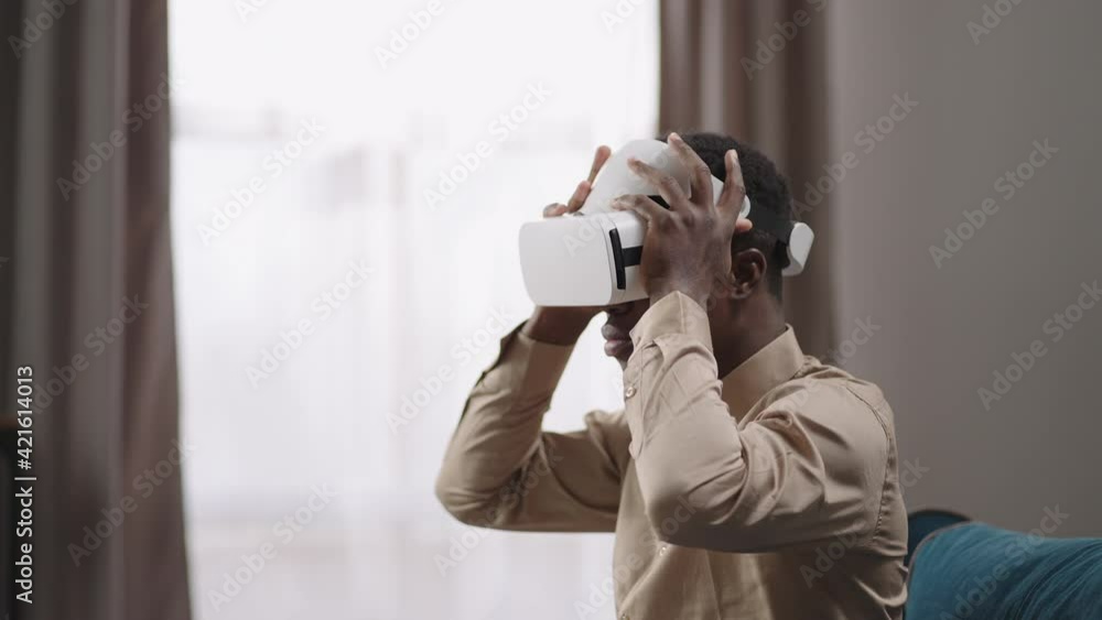 afro-american guy is putting head-mounted display off sitting at home, using vr glasses at home for education and entertainment afro-american guy is putting head-mounted display off sitting at home, using vr glasses at home for education and entertainment