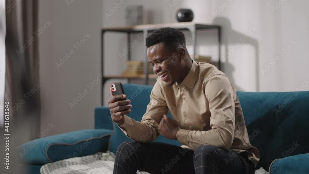 happy afro-american teen is using app for video call in smartphone, sitting alone at home, laughing and talking with friends happy afro-american teen is using app for video call in smartphone, sitting alone at home, laughing and talking with friends