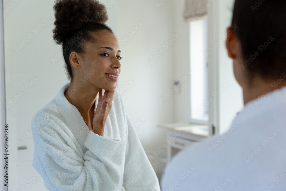 Mixed race woman wearing bathrobe and looking in a mirror in bathroom Mixed race woman wearing bathrobe and looking in a mirror in bathroom