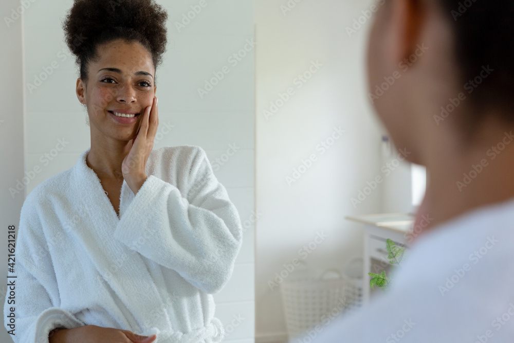 Mixed race woman wearing bathrobe and looking in a mirror in bathroom Mixed race woman wearing bathrobe and looking in a mirror in bathroom