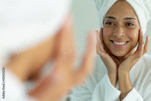 Mixed race woman wearing bathrobe and cleansing face mask in bathroom