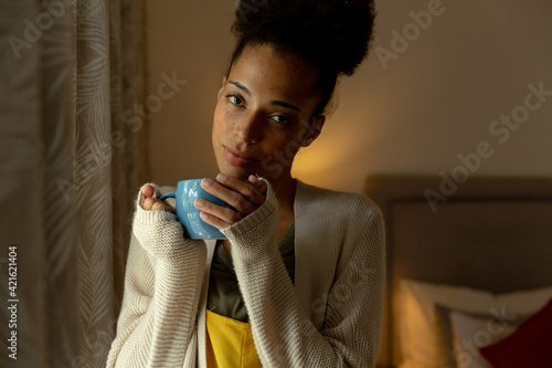 Mixed race woman standing by a window and drinking cup of coffee at home