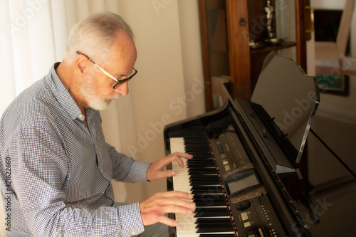 Man practicing playing the piano in the living room of his home after retirement from work. © Danko