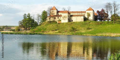 Amazing panorama of Svirzh medieval castle, reflected in water of nearby lake under high blue sky with clouds