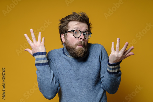 The strange, surprised man shrugs his shoulders and makes a bewildered hand gesture. Yellow background. photo