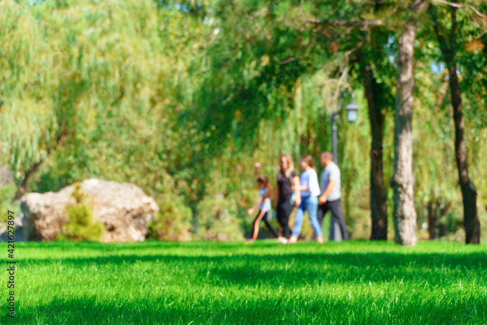 Obraz premium people walking and children playing in a city park on a summer day, green lawns with grass and trees, paths and benches, bright sunlight and shadows