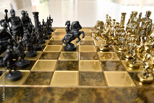 Fotografija Black and gold metal knight chess figurines on horseback attacking on chessboard