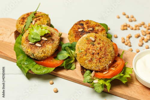 Lean falafel sandwiches, mixed salad and tomato slices, on a wooden board with sauce in a bowl. Close-up on a light background photo