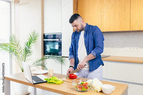 A young man spends the day at home, preparing breakfast in the kitchen with vegetables, a man in home clothes and with a beard