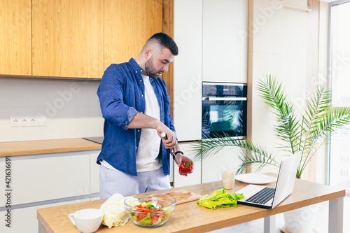 A young man spends the day at home, preparing breakfast in the kitchen with vegetables, a man in home clothes and with a beard