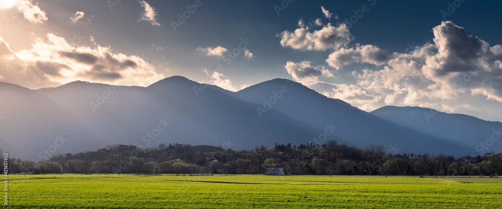Obraz premium ultime luci del giorno sulla piana di rieti vista dal lago di ripasottile. campi verdi illuminati dai raggi caldi del sole