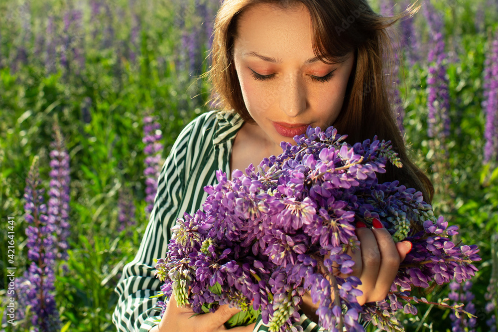 beautiful girl looking at lupine armful in her hands on background of blooming lupine field. Natural style golden makeup. Fashion, beauty, make-up, cosmetics, beauty salon, style. perfumes, perfumery beautiful girl looking at lupine armful in her hands on background of blooming lupine field. Natural style golden makeup. Fashion, beauty, make-up, cosmetics, beauty salon, style. perfumes, perfumery