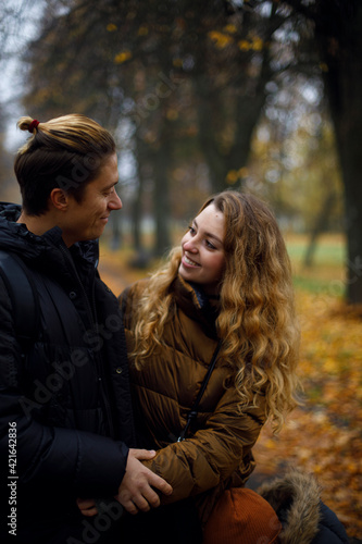 Caucasian guy with a girl laugh and smile looking at each other. young happy couple hugging in the park with yellow leaves on the background. friendship between a guy and a girl