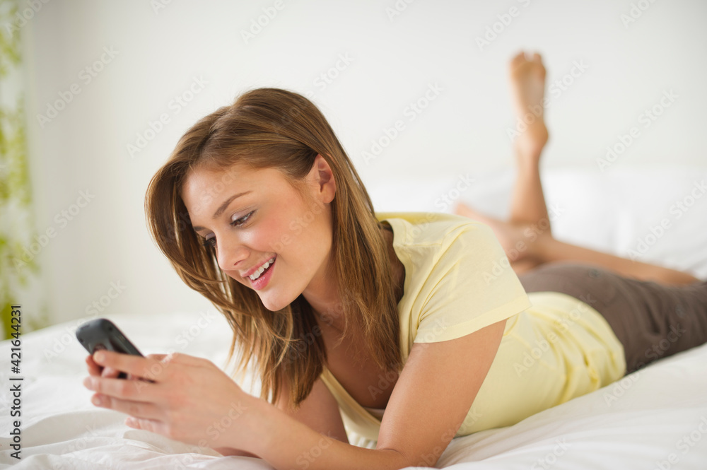 USA, New Jersey, Jersey City, Young woman lying on bed with mobile phone USA, New Jersey, Jersey City, Young woman lying on bed with mobile phone