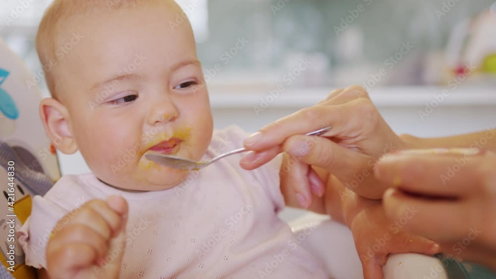 Woman feeding child with spoon. Mom feed baby with pureed food. Mom feeding kid in baby chair. Woman feeding child with spoon. Mom feed baby with pureed food. Mom feeding kid in baby chair.