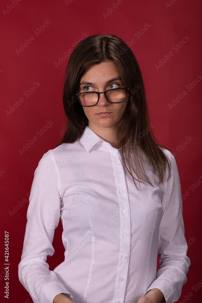 tired exhausted long-haired brunette girl in glasses and white shirt looks focused and tense posing on red studio backdrop. anxiety, family problems, gender discrimination, Office fatigue concept