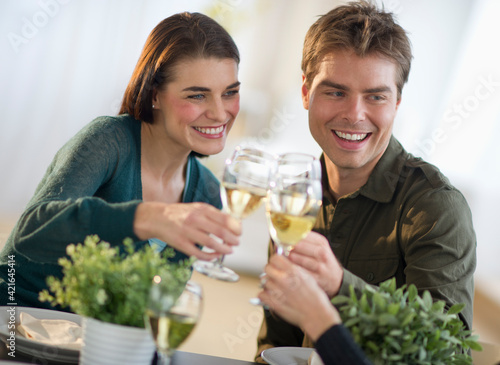 Couple toasting with white wine with third party in background photo