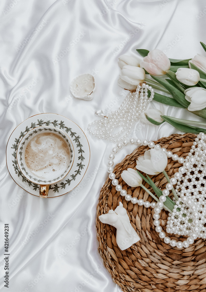 White tulips, coffee cup and woman accessory on silk background, Morning coffee cup spring mood. Luxury romantic background. Woman morning, aesthetic concept. Top view, flat lay White tulips, coffee cup and woman accessory on silk background, Morning coffee cup spring mood. Luxury romantic background. Woman morning, aesthetic concept. Top view, flat lay