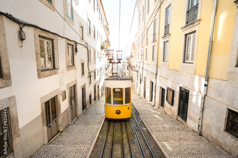 Trams in Lisbon city. Famous retro yellow funicular tram on narrow streets of Lisbon old town on a sunny summer day. Tourist attraction