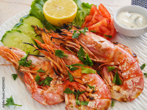 large shrimps with vegetables, lemon and sauce on a white dish