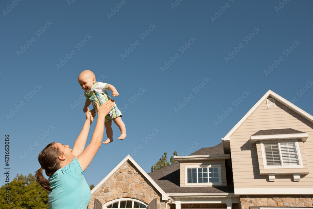 Mother lifting baby boy (6-11 months) outside home Mother lifting baby boy (6-11 months) outside home