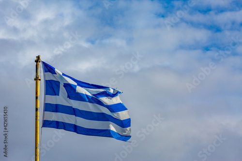 Greek flag, yellow metallic rod, on puffy white clouds sky background. Picture taken at Meteora, Greece.