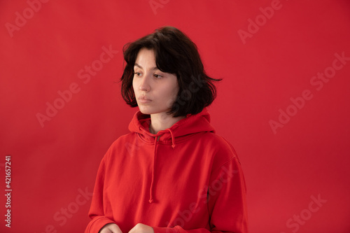 tired brunette Girl in red hoodie posing on red studio backdrop copy space. Pain, fatigue, tension concept. Loneliness, desire talk to someone. Psychotherapist, psychologist, relationship correction