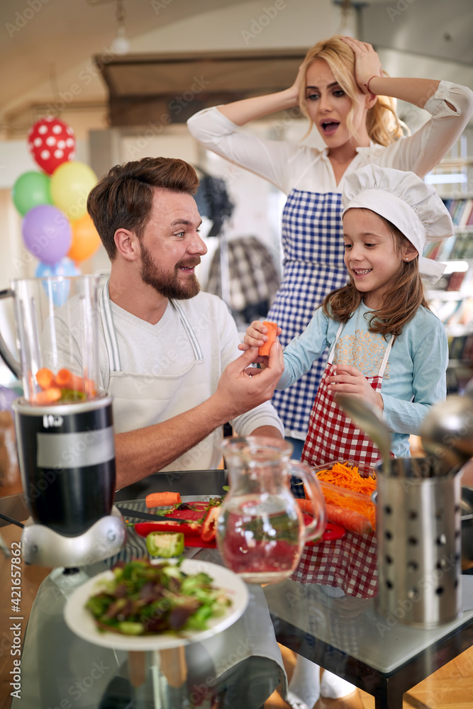 A young mother is worried that her husband and little daughter will destroy a meal they are preparing at home. Family, home, kitchen A young mother is worried that her husband and little daughter will destroy a meal they are preparing at home. Family, home, kitchen
