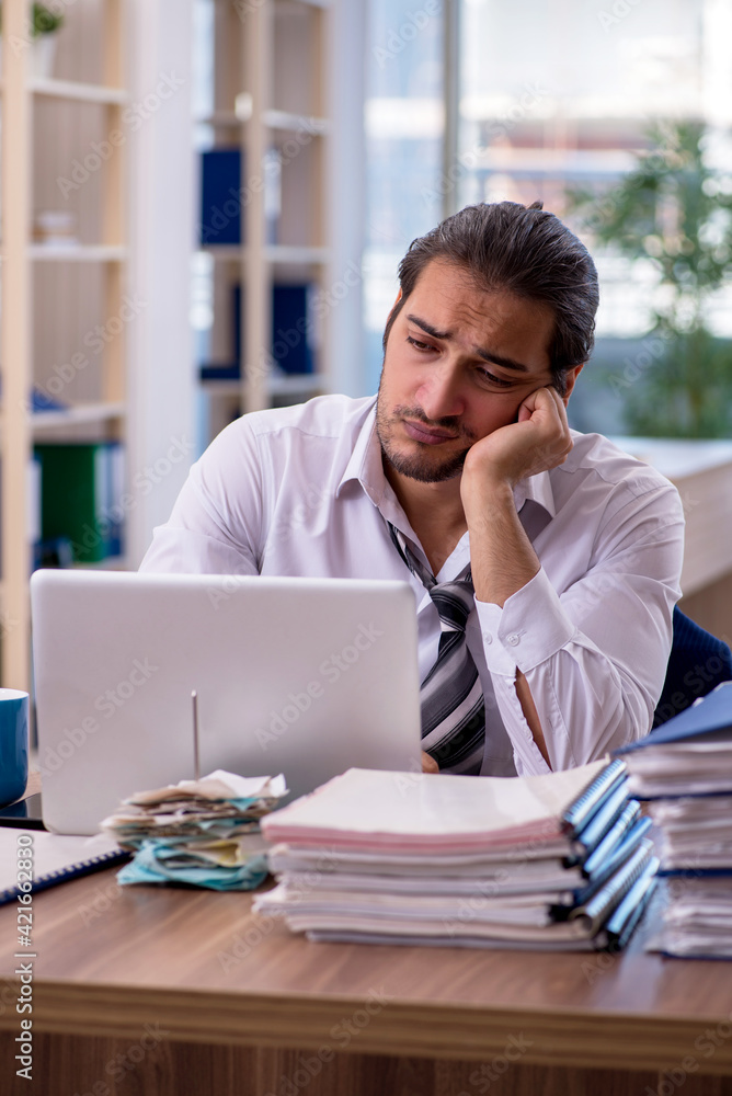 Young male employee unhappy with excessive work in the office Young male employee unhappy with excessive work in the office