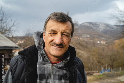 Portrait of senior caucasian man in nature standing in spring or autumn day - close up of cheerful male farmer standing in rural nature on farm looking to the camera - real people concept