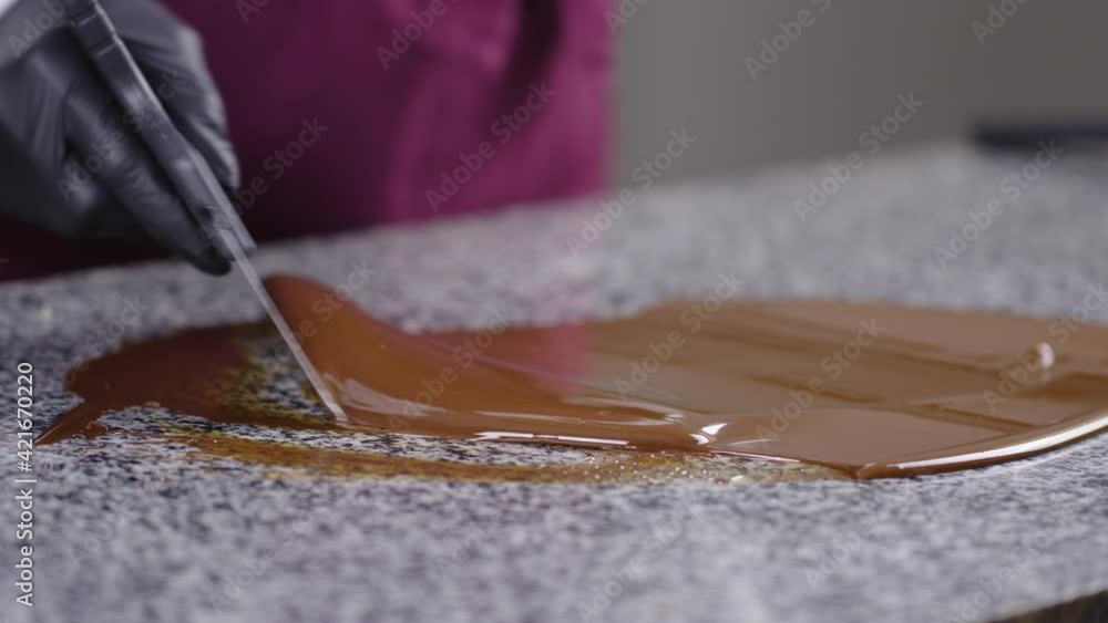 tempering of melted chocolate on granite table close up selective focus. Chocolatier stirring tempered liquid chocolate with spatula side view. tempering of melted chocolate on granite table close up selective focus. Chocolatier stirring tempered liquid chocolate with spatula side view.