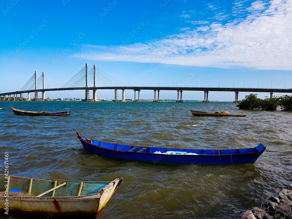 Barcos de pesca artesanal ancorados em um rio com uma ponte ao fundo