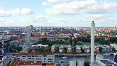 Stockholm, Sweden. Aerial Drone summer view of a beautiful canal and bay at Hammarby Sjöstad with modern architecture, marina, houseboats, an industry with white chimney, and skyline with high towers.