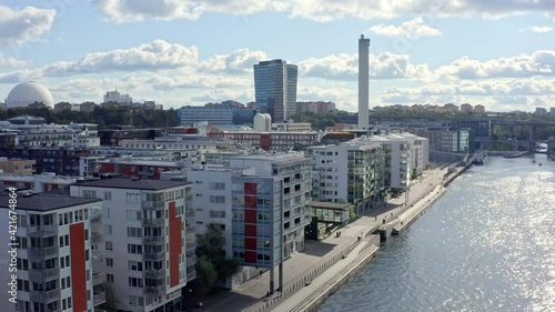 Stockholm, Sweden. Aerial Drone summer view of a beautiful boardwalk, canal and bay at Hammarby Sjöstad with modern architecture, boardwalk, boats, skyscraper, white chimney and globe structure.