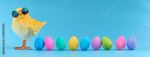 Fotografia Easter decoration of a yellow chick wearing silly sunglasses with a row of colorful painted Easter eggs