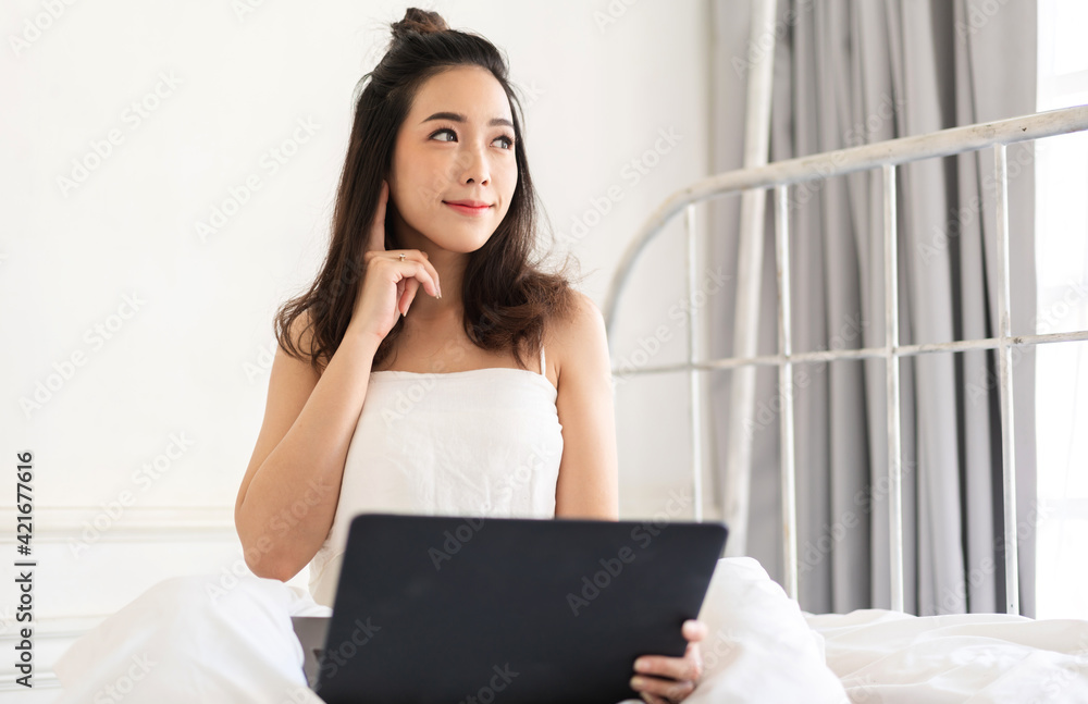 Young smiling happy beautiful asian woman relaxing using laptop computer in the bedroom at home.Young creative girl working and typing on keyboard.work from home concept Young smiling happy beautiful asian woman relaxing using laptop computer in the bedroom at home.Young creative girl working and typing on keyboard.work from home concept