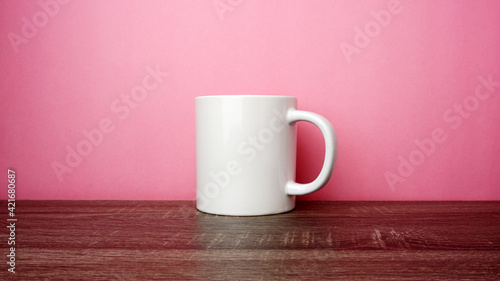 Empty white cup on top of the wooden table on pink background. 
