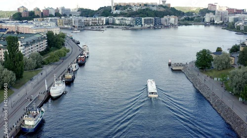 Stockholm, Sweden. Aerial Drone hovering still with a summer view of a lake and bay at Hammarby Sjöstad with modern architecture, sightseeing boat, and docks with old houseboats.