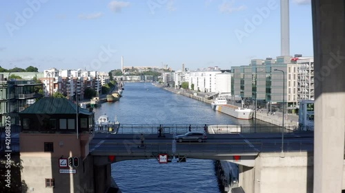 Summertime, Stockholm, Sweden. Aerial drone flying under a bridge with a lock, scooters, people, canal and bay at Hammarby Sjöstad with modern architecture, marina, and old boats.