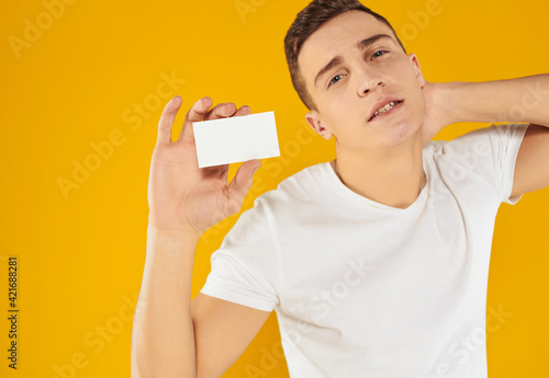 man in white t-shirt showing business card on yellow background cropped view